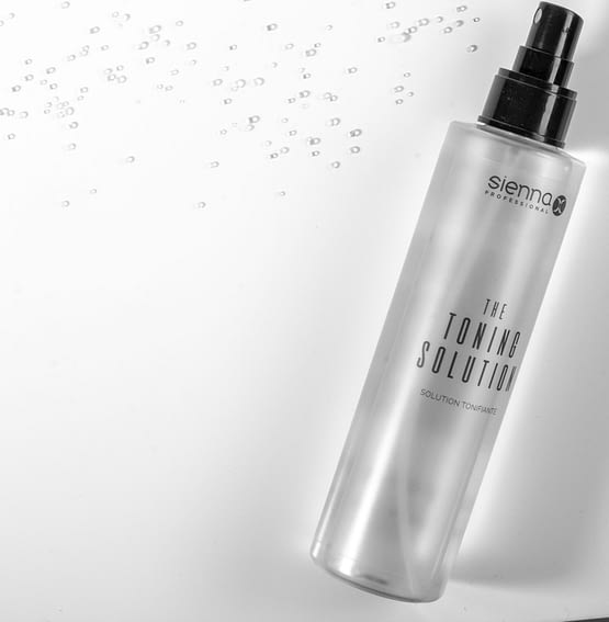 the toning solution by sienna x. The image shows a clear bottle with toning product inside, with a black pump spray applicator top. The product is laid down. All sienna x packaging is recyclable.