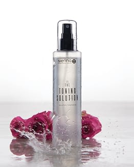 the toning solution by sienna x. The image shows a clear cylindrical bottle stood up with a black spray applicator and clear lid.
